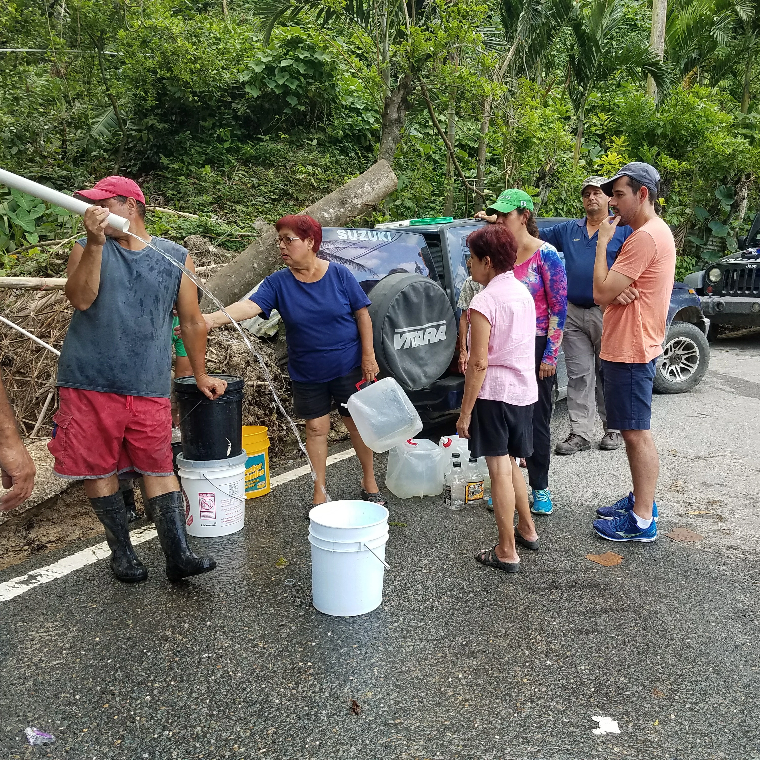 Personas observando cómo sale agua de una tubería para recoger agua